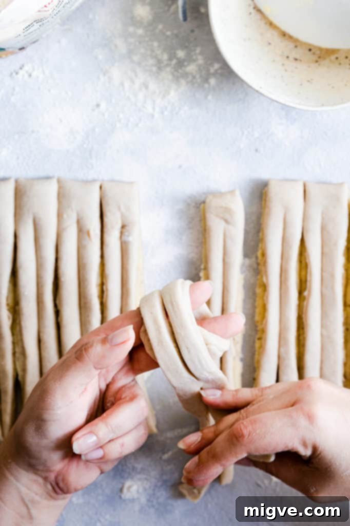 Overhead shot of a baker's hands expertly shaping the dough into a knot for a cardamom bun.