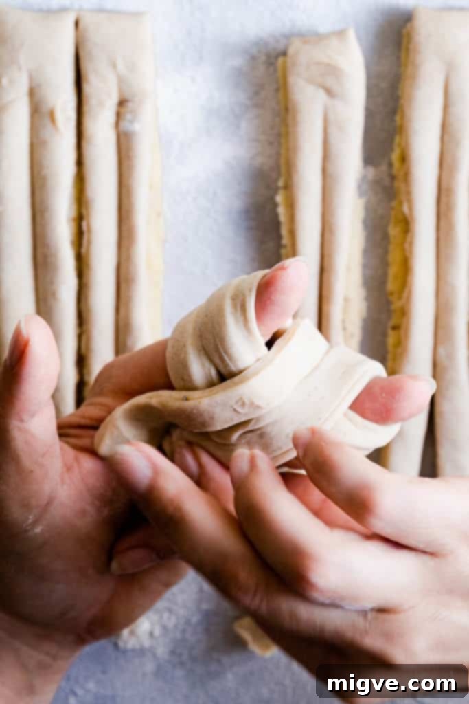 Close-up of hands expertly twisting and shaping the dough to create the signature cardamom bun knot.