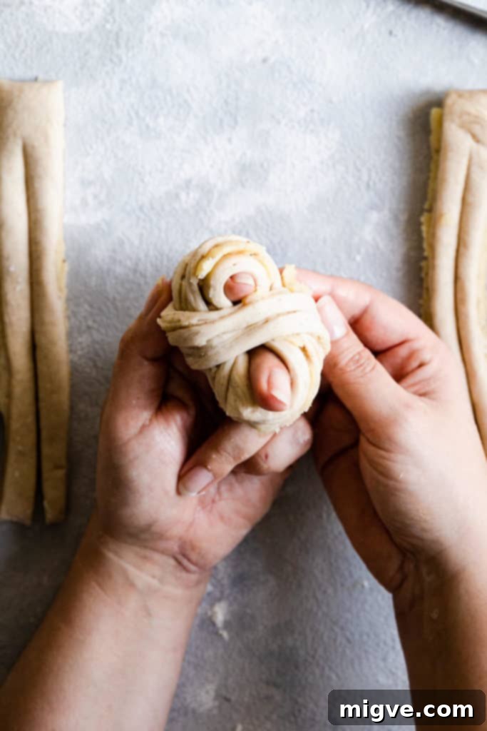 Top-down view of hands completing the knot shape for a cardamom bun, tucking the ends underneath.