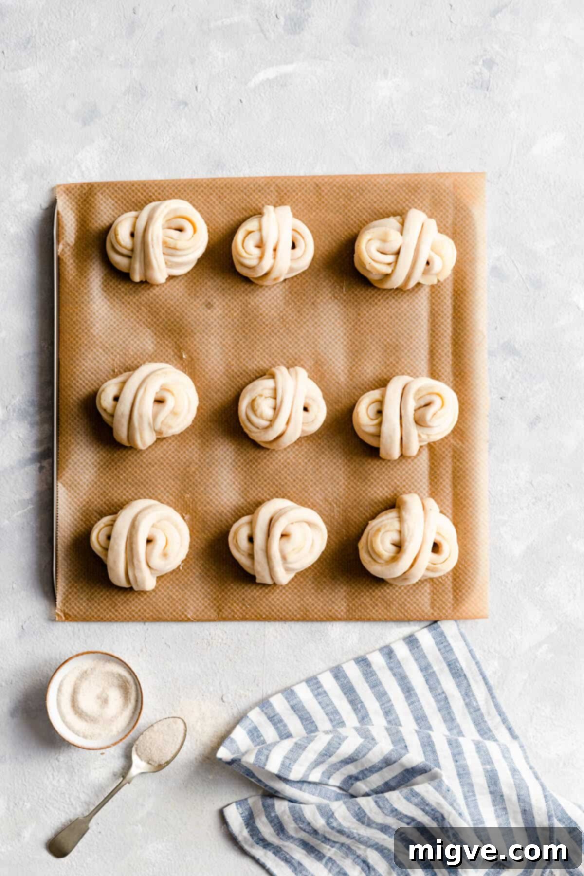 Top-down view of unbaked cardamom buns, egg-washed and topped with sugar pearls, resting on a baking tray before going into the oven.