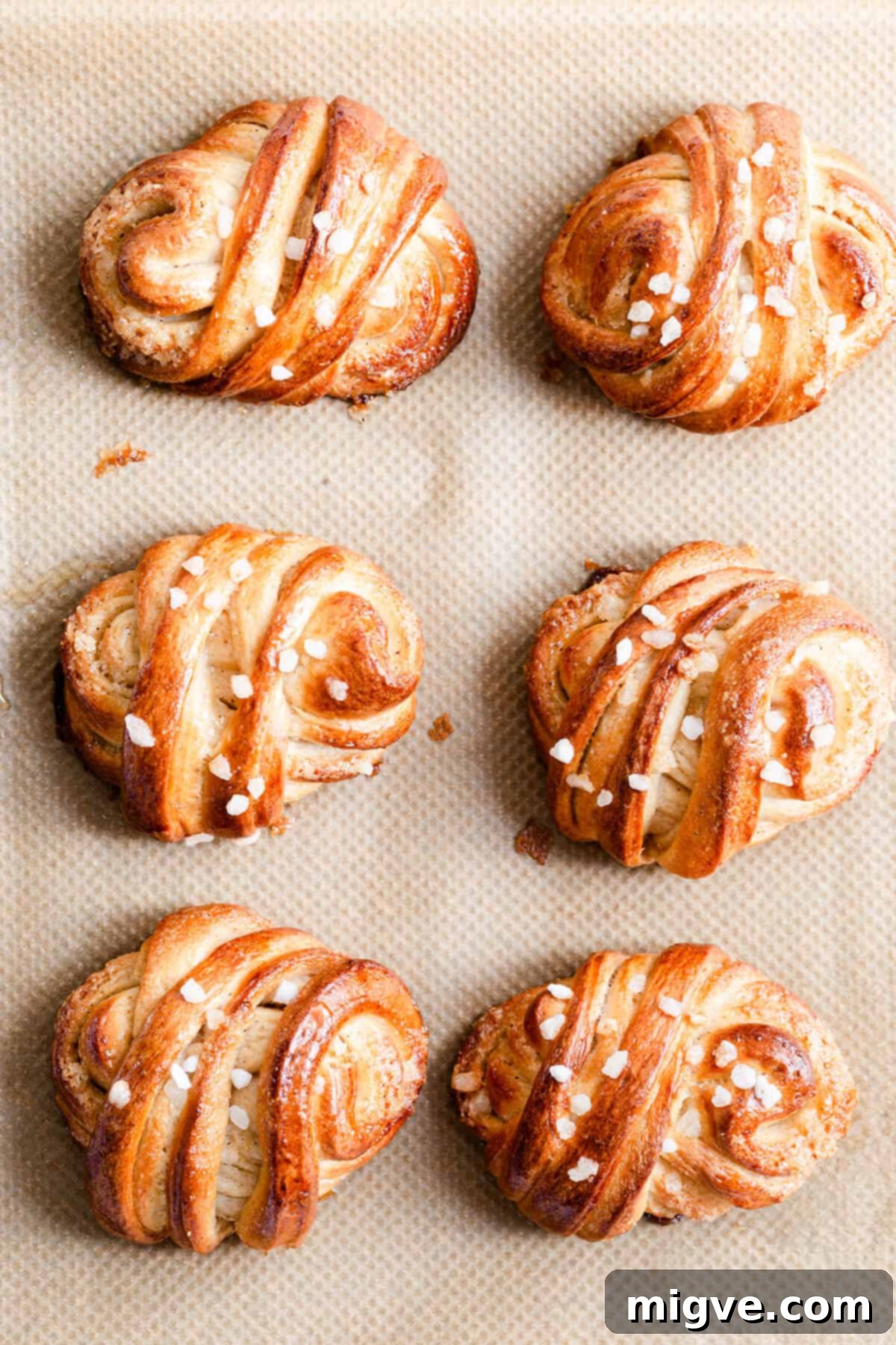 Top-down view of freshly baked Swedish cardamom buns, glistening with syrup, cooling on a rack.
