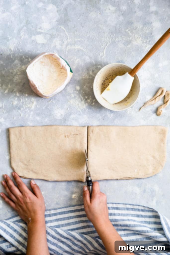 Overhead shot of a person using a pizza cutter to slice the dough into strips for cardamom buns.
