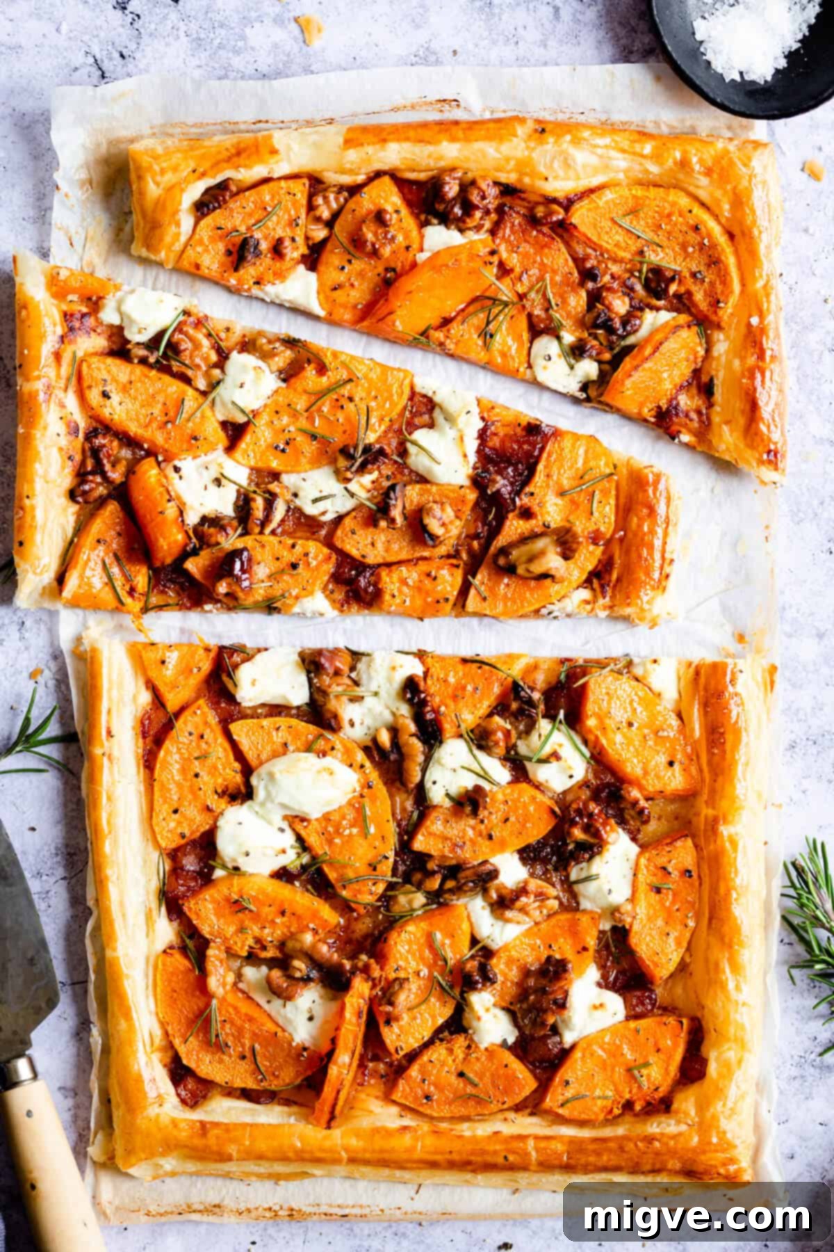 Close-up, top-down view of a beautifully sliced butternut squash and goats' cheese tart, garnished with fresh rosemary and crunchy walnuts, ready to be served as a delightful vegetarian meal.