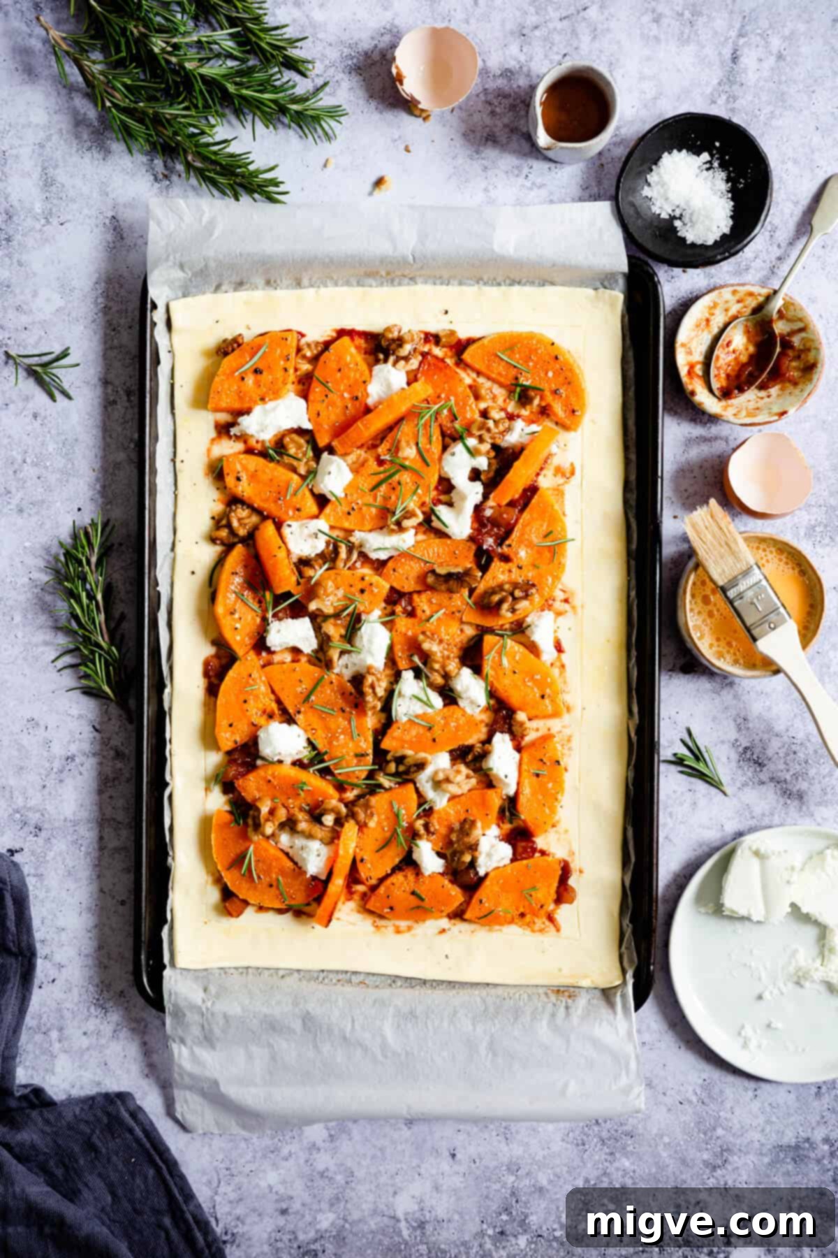 Overhead shot of an unbaked butternut squash and goats' cheese tart, fully assembled on a baking tray, showcasing its vibrant ingredients before going into the oven.
