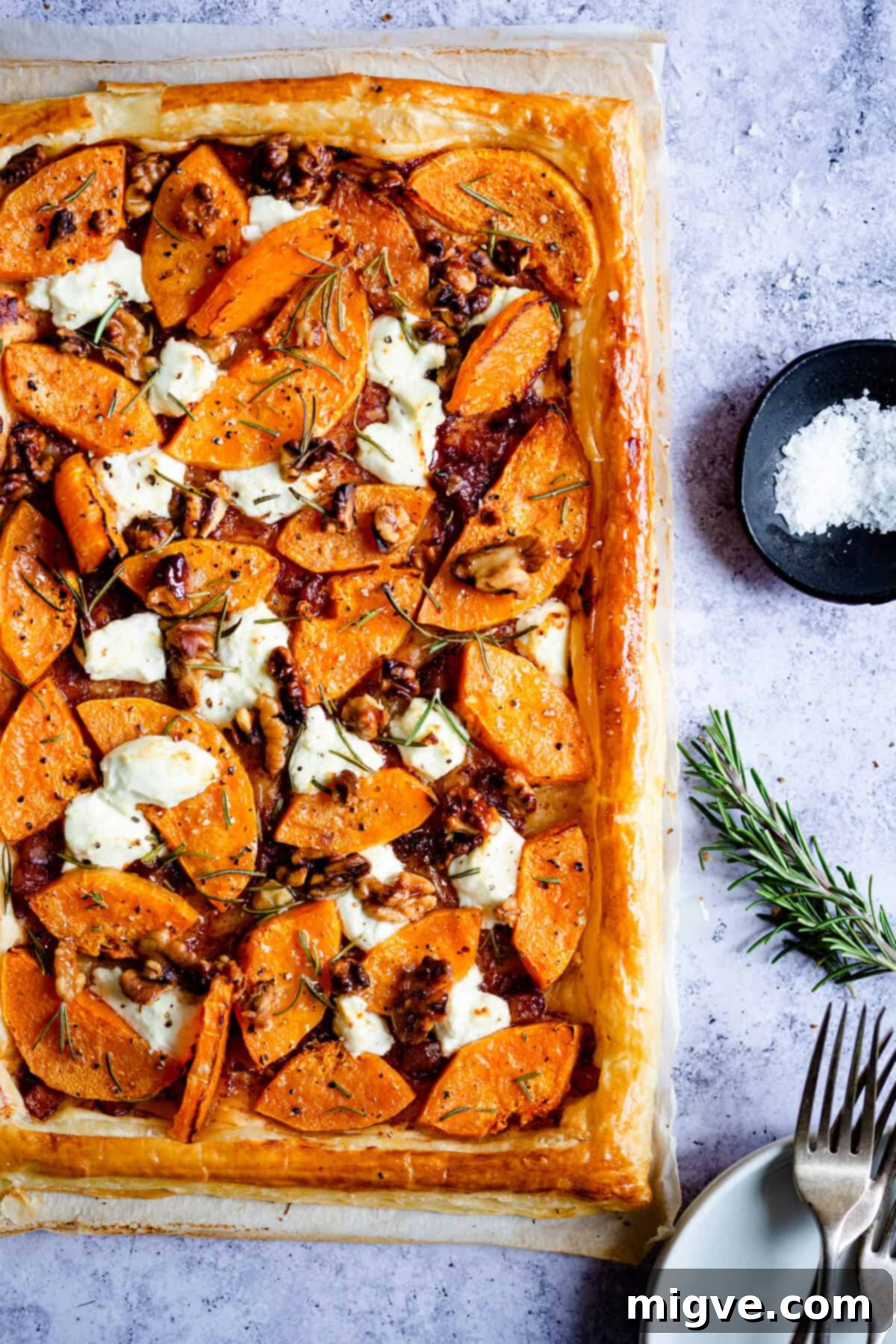 Close-up of the freshly baked butternut squash and goats' cheese tart, with a perfectly golden crust, melted cheese, and tender squash pieces glistening with olive oil and rosemary.