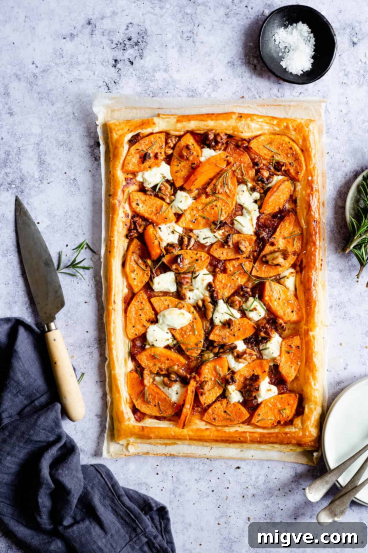 Overhead shot of a golden puff pastry tart generously topped with roasted butternut squash, creamy goats' cheese, and fresh herbs, showcasing its rustic homemade appeal.