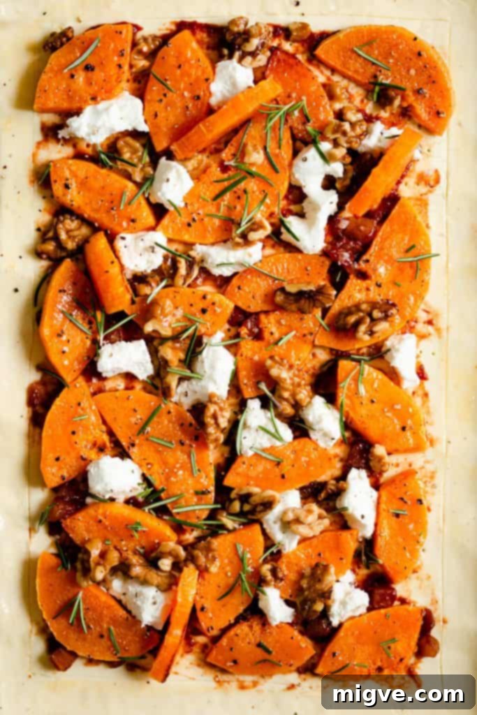 Close-up view of a golden-baked butternut squash tart, highlighting the melted goats' cheese, perfectly roasted squash pieces, and aromatic fresh rosemary sprigs.
