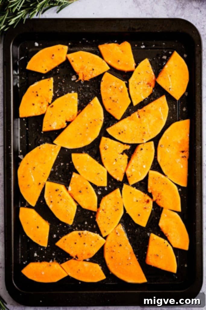 Top-down view of a baking tray filled with perfectly roasted butternut squash wedges, seasoned and slightly golden, ready to be added to the tart.