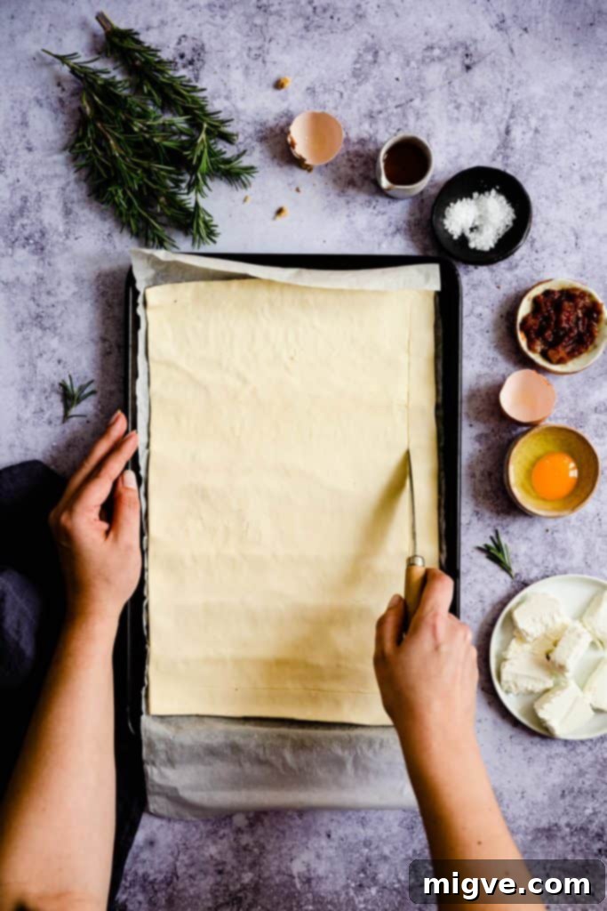 Overhead shot of a person gently scoring the edges of pre-rolled puff pastry on a baking sheet, creating a neat border for the tart.