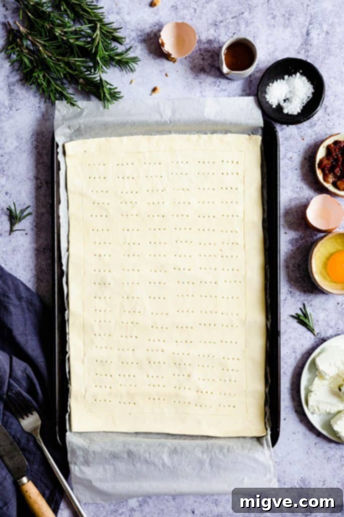 Top-down view of a ready-rolled puff pastry sheet lying flat on a baking tray, with its edges neatly scored, preparing it for the tart fillings.