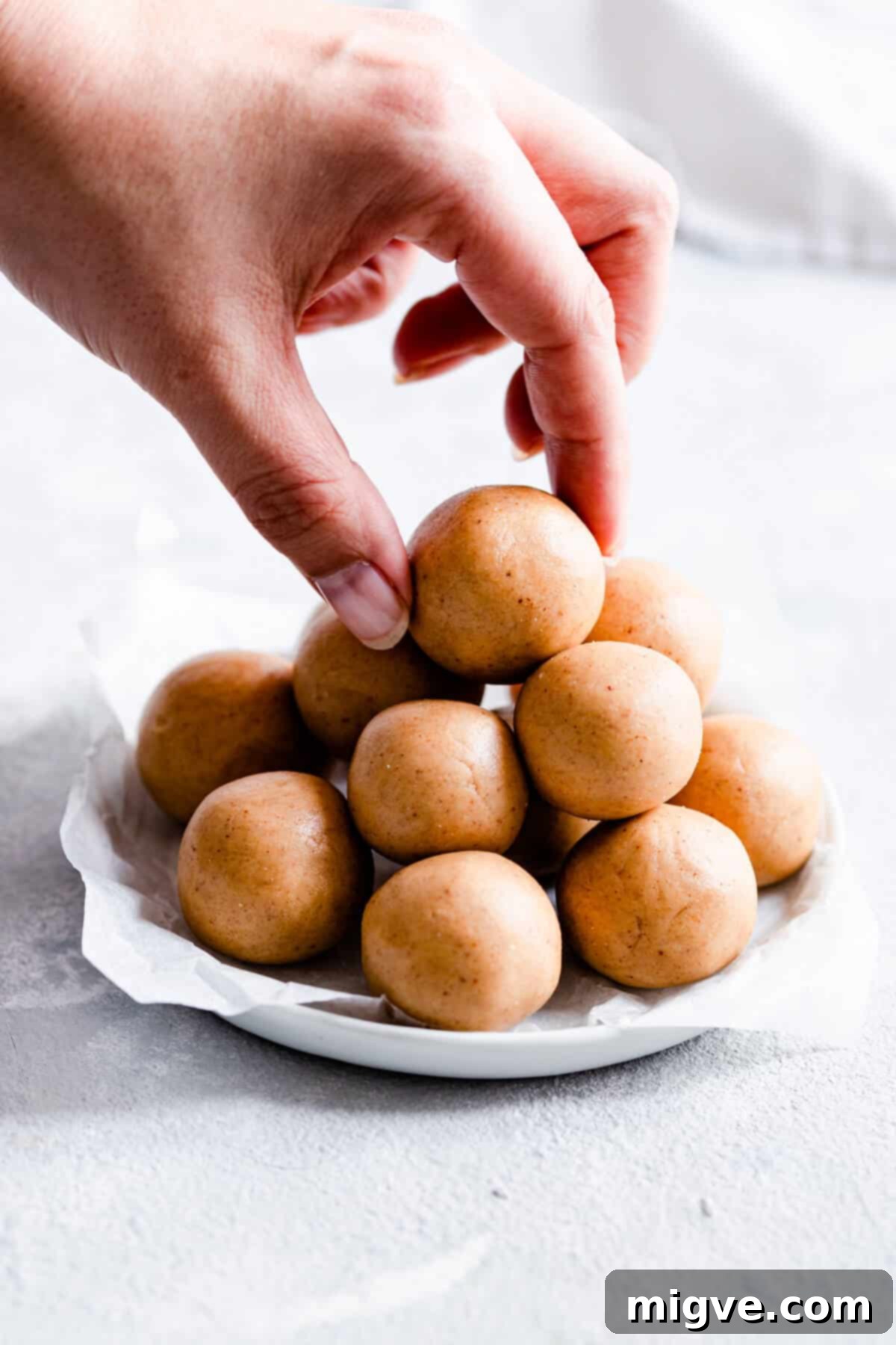 A close-up shot of a hand reaching out to grab a peanut butter energy bite from a small stack, emphasizing their grab-and-go appeal.