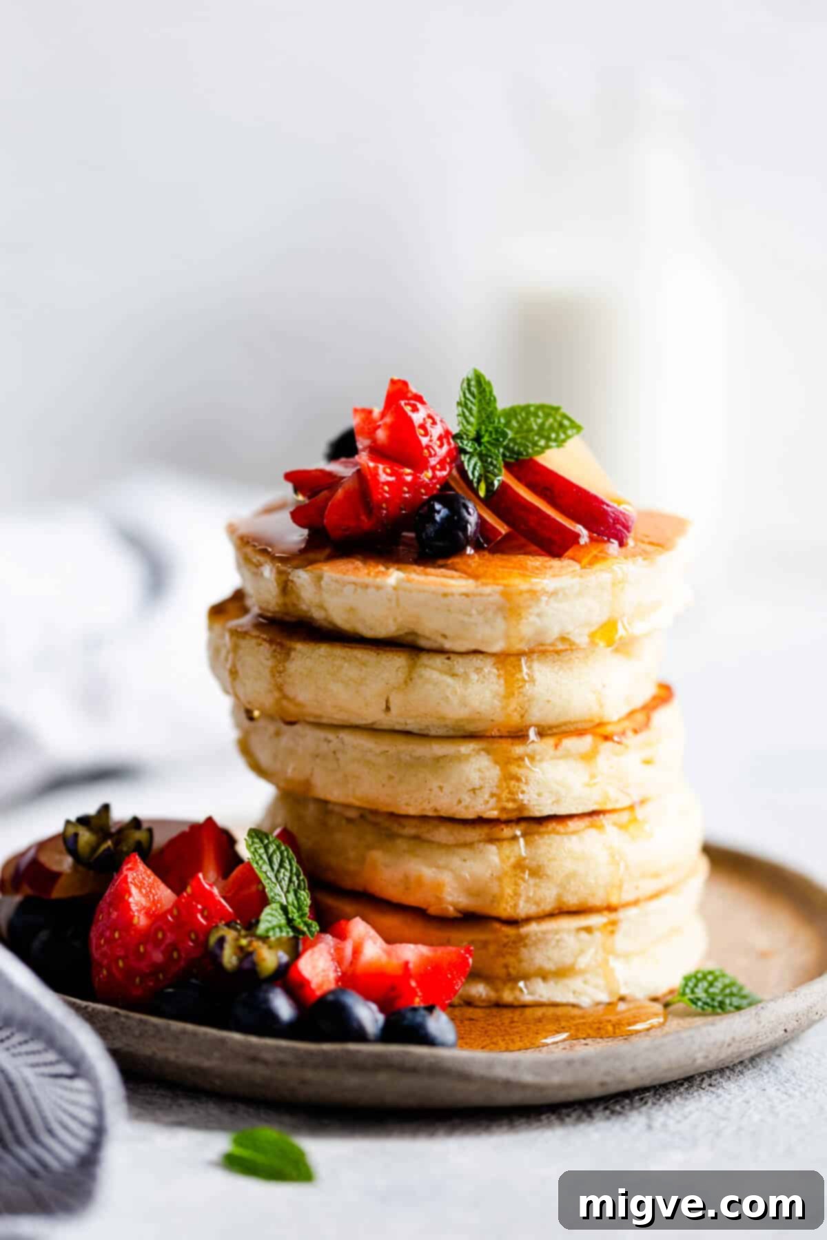 A close-up side view of a tall stack of five perfectly fluffy pancakes, golden brown and ready to be served.
