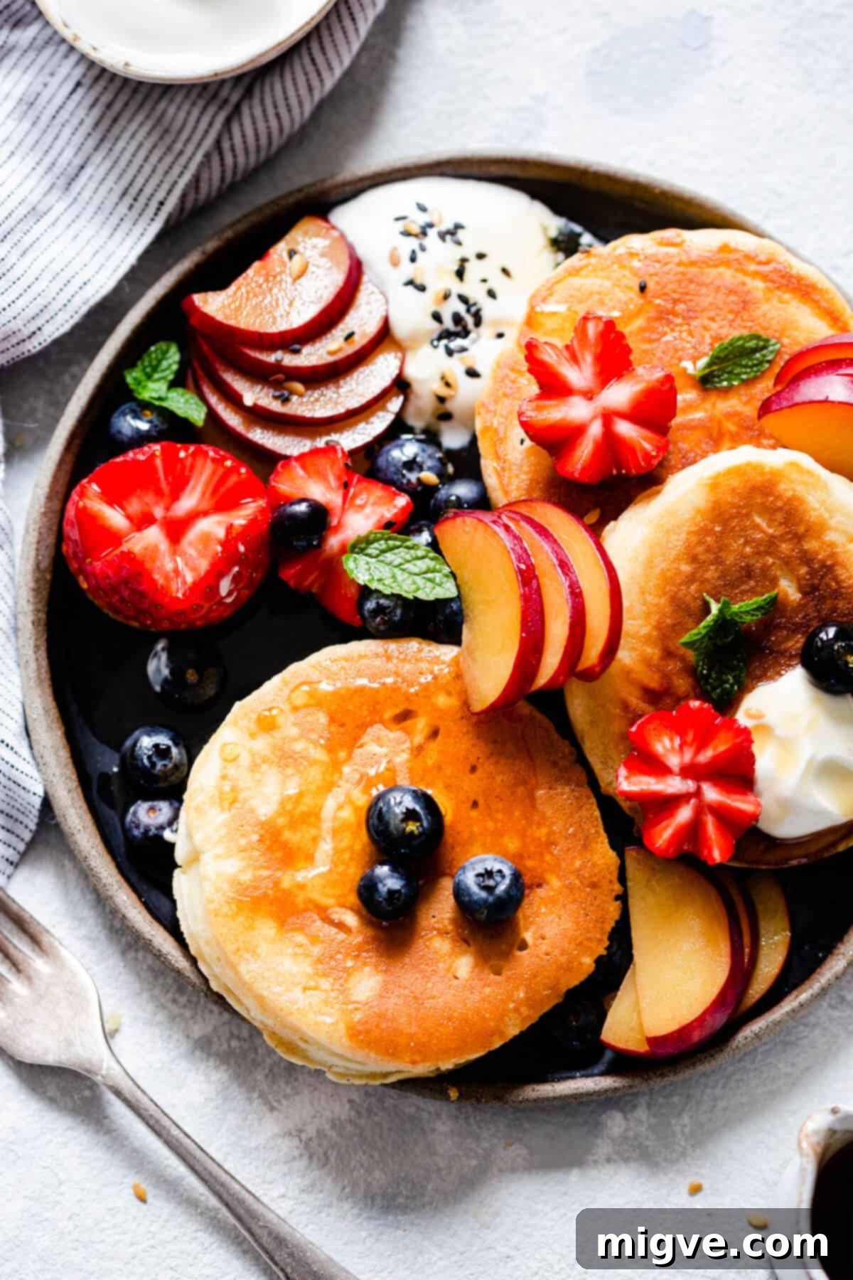 Overhead shot of a plate laden with golden fluffy pancakes, accompanied by a vibrant selection of fresh fruits like berries and sliced banana.