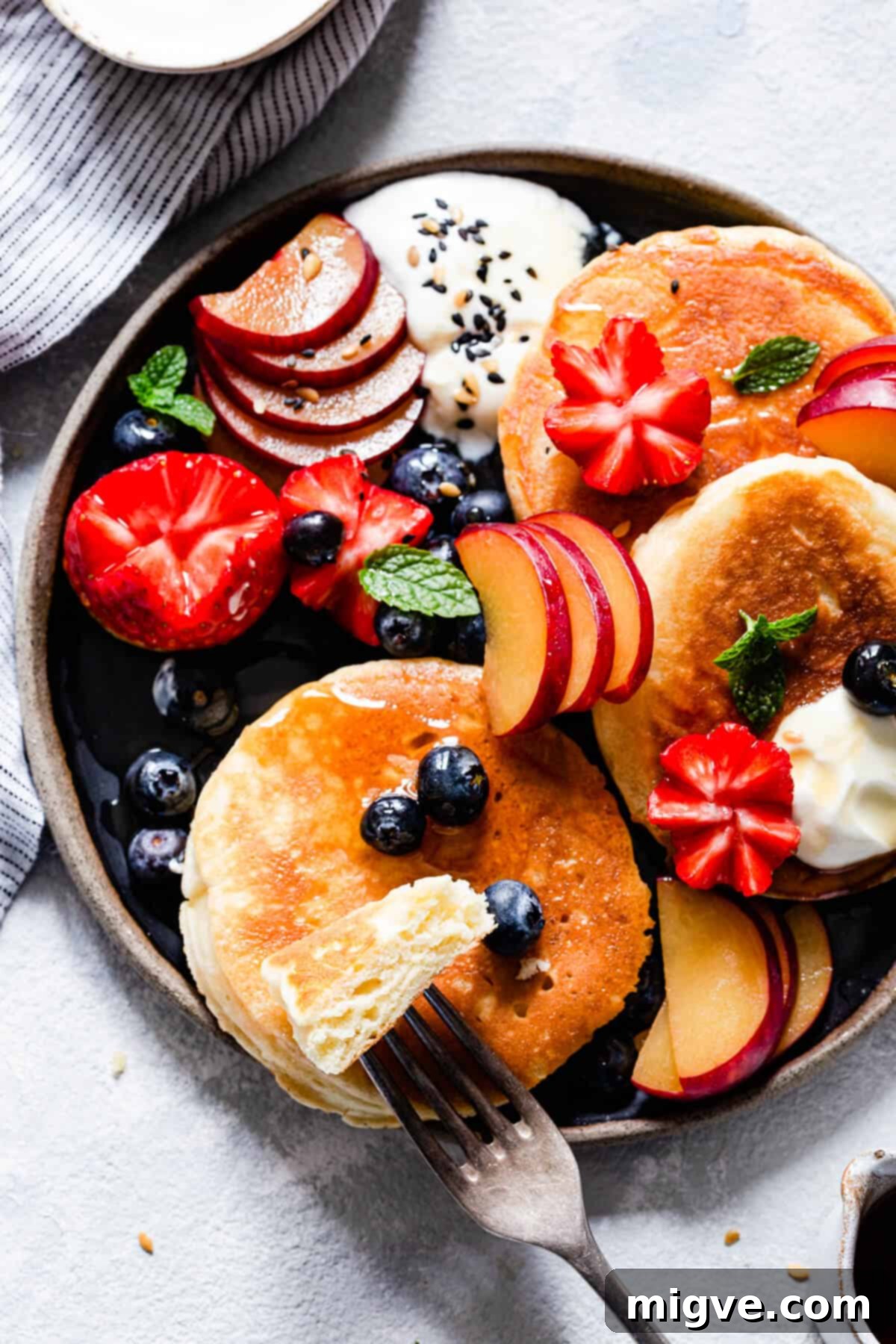Top view of a plate with a stack of fluffy pancakes, a pat of butter, and a fork holding a sliced piece of pancake.
