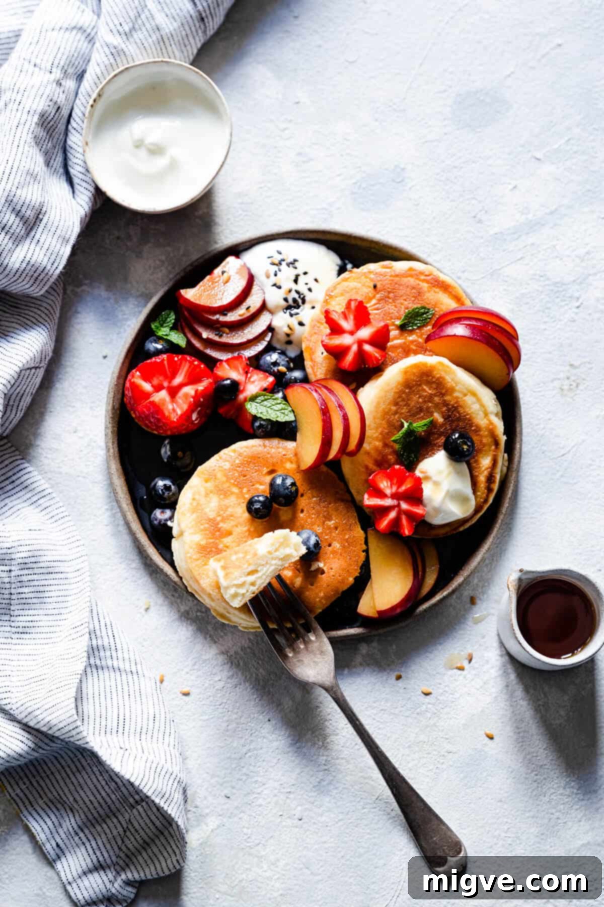 Overhead shot of a plate with a stack of golden fluffy pancakes and a small pitcher of maple syrup on the side.