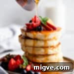 Maple syrup being poured generously over a fresh stack of fluffy pancakes, ready to be served.