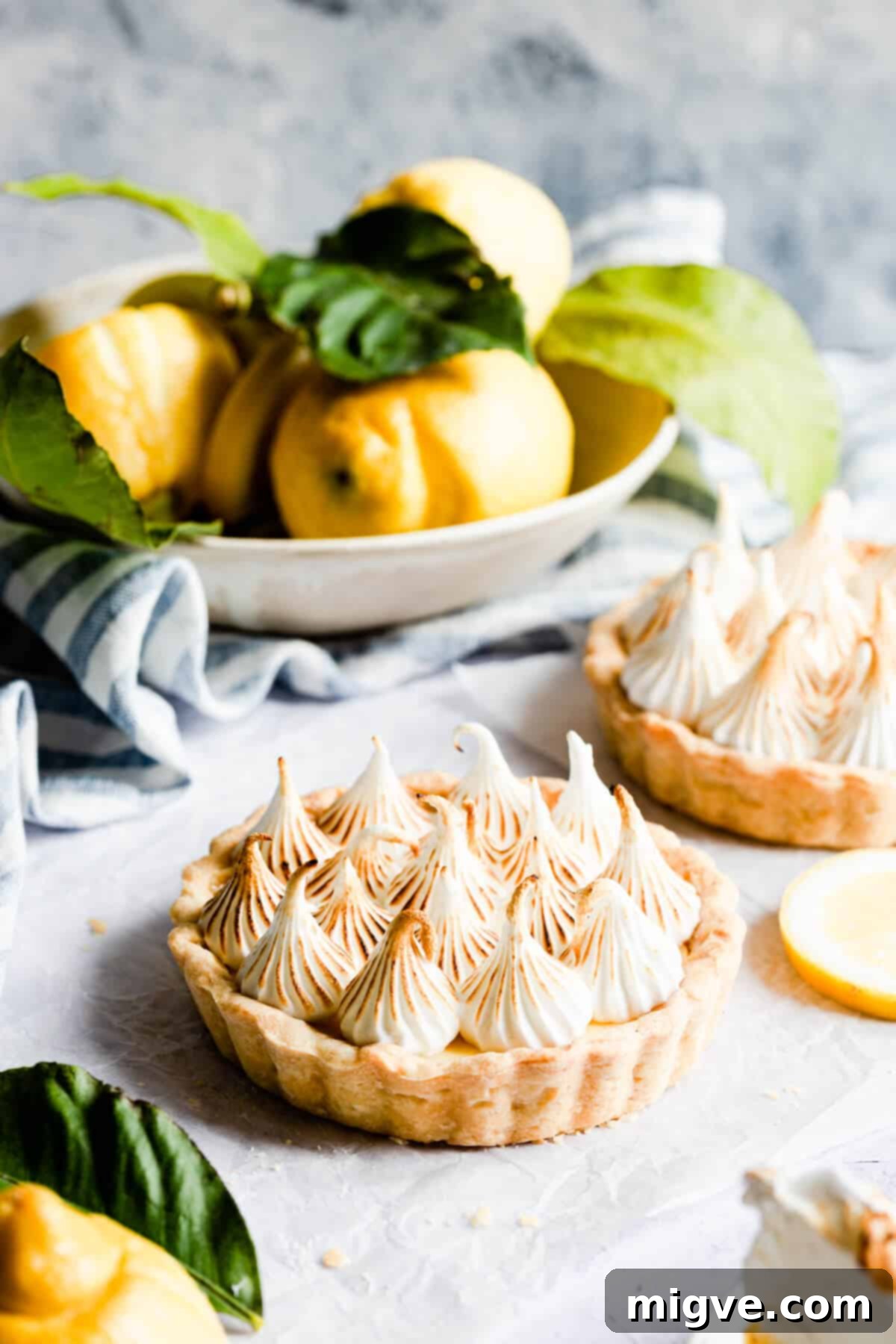 A close-up side view of a small, perfectly baked lemon meringue pie, showcasing its golden crust, creamy lemon filling, and towering, fluffy Italian meringue topping. Ideal for any celebration or a sweet treat.