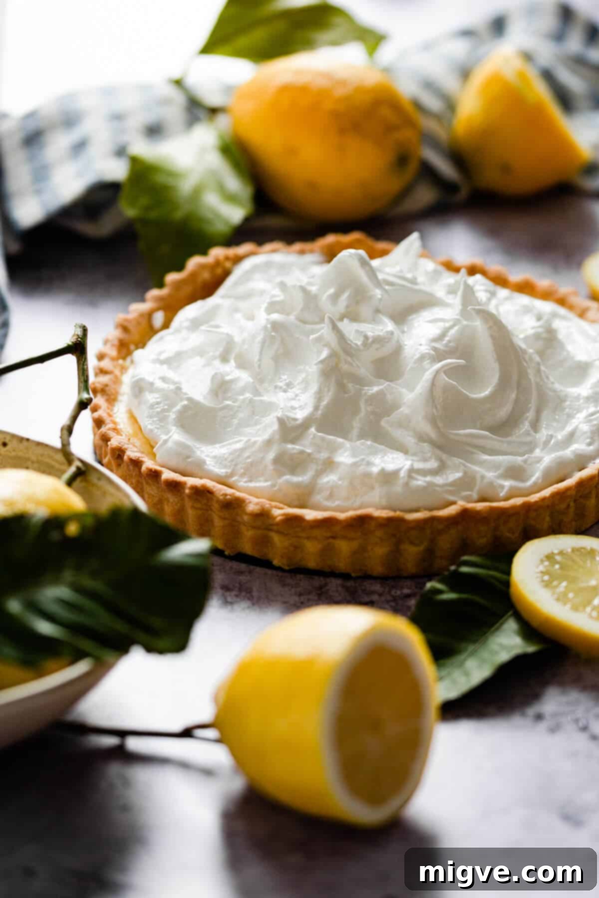 A striking side angle of a whole lemon meringue pie, featuring its golden crust and dramatic, toasted meringue peaks.