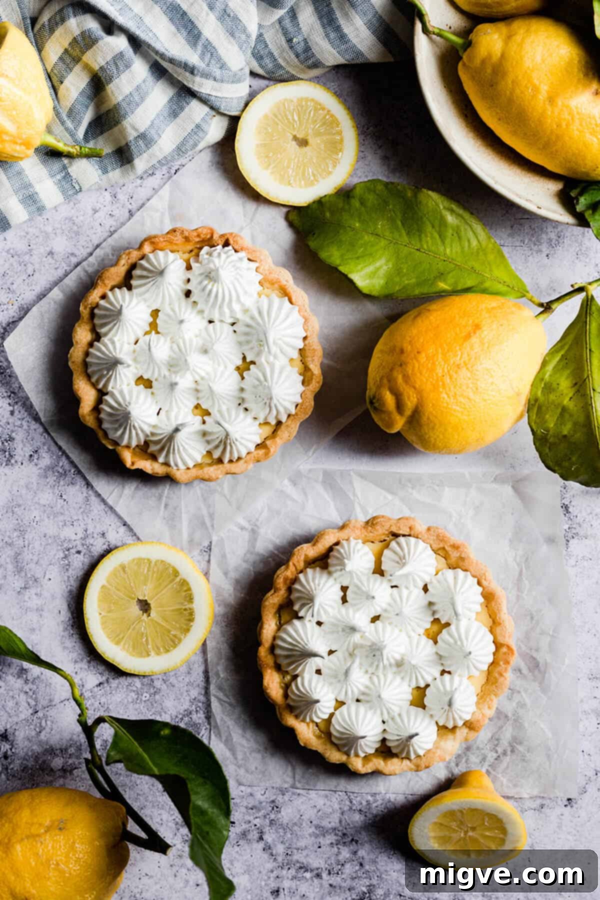 An overhead view of two smaller, individual lemon meringue pies, each adorned with beautifully swirled and toasted meringue peaks, ready for serving.