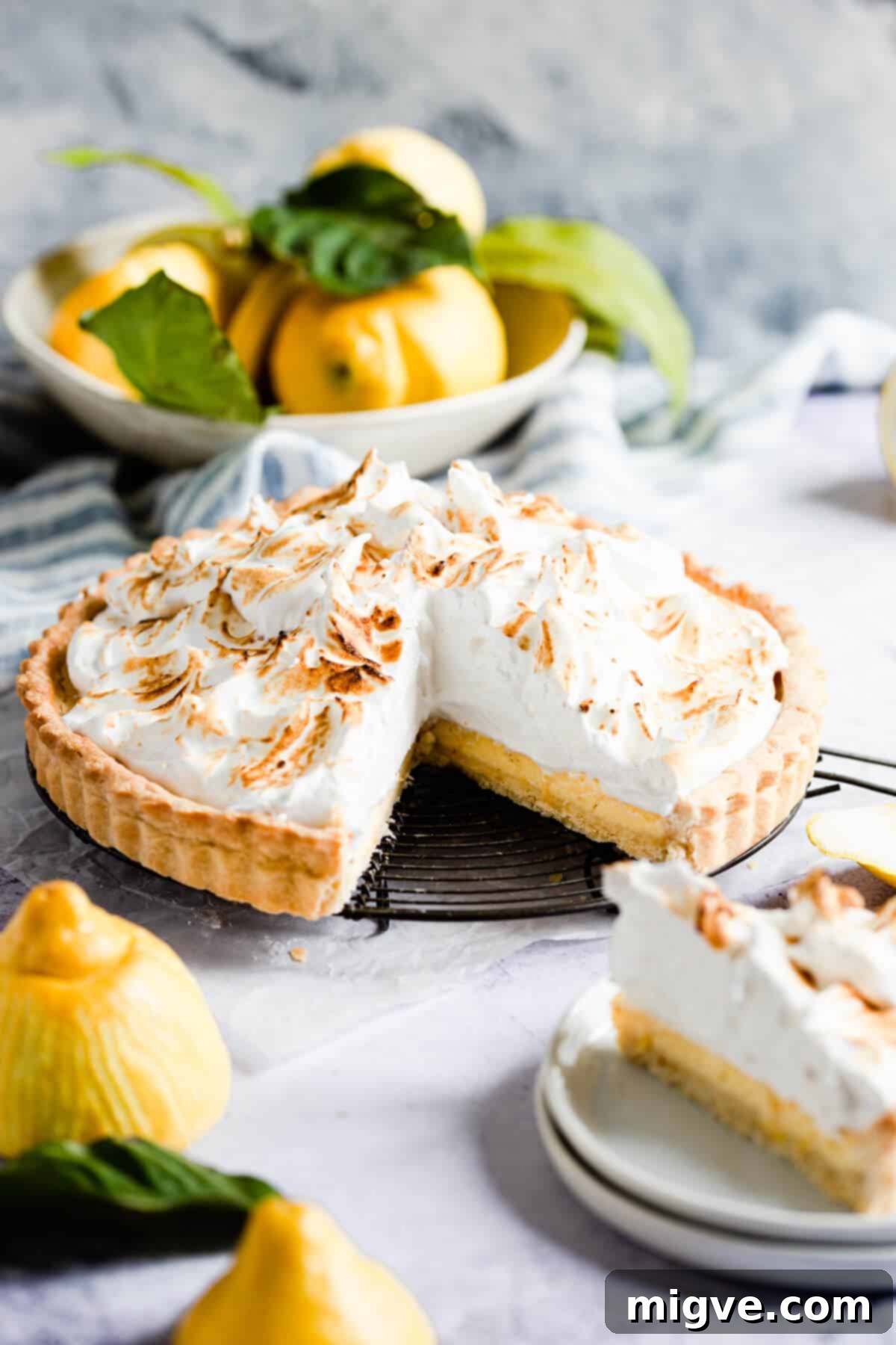 A side view of a slice of classic lemon meringue pie, showcasing the crisp shortcrust, bright lemon filling, and tall, fluffy meringue topping.