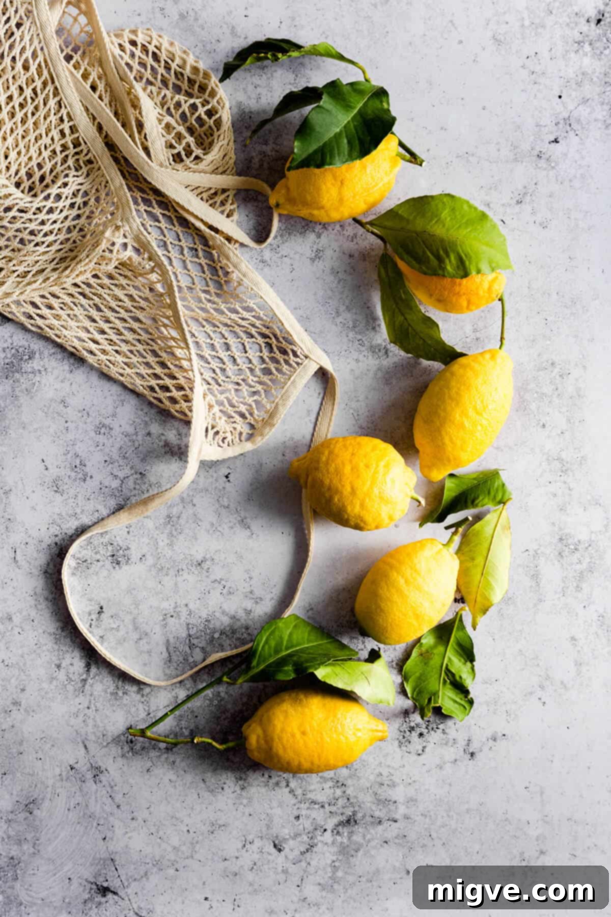 A top-down view of several fresh, whole lemons scattered loosely on a surface, highlighting their bright yellow color and bumpy texture.