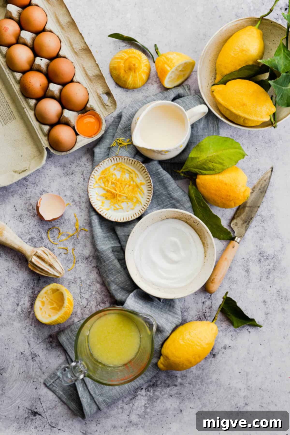 A top-down view of the fresh ingredients for the lemon pie filling, including whole lemons, eggs, and a bowl of cream, arranged on a rustic surface.