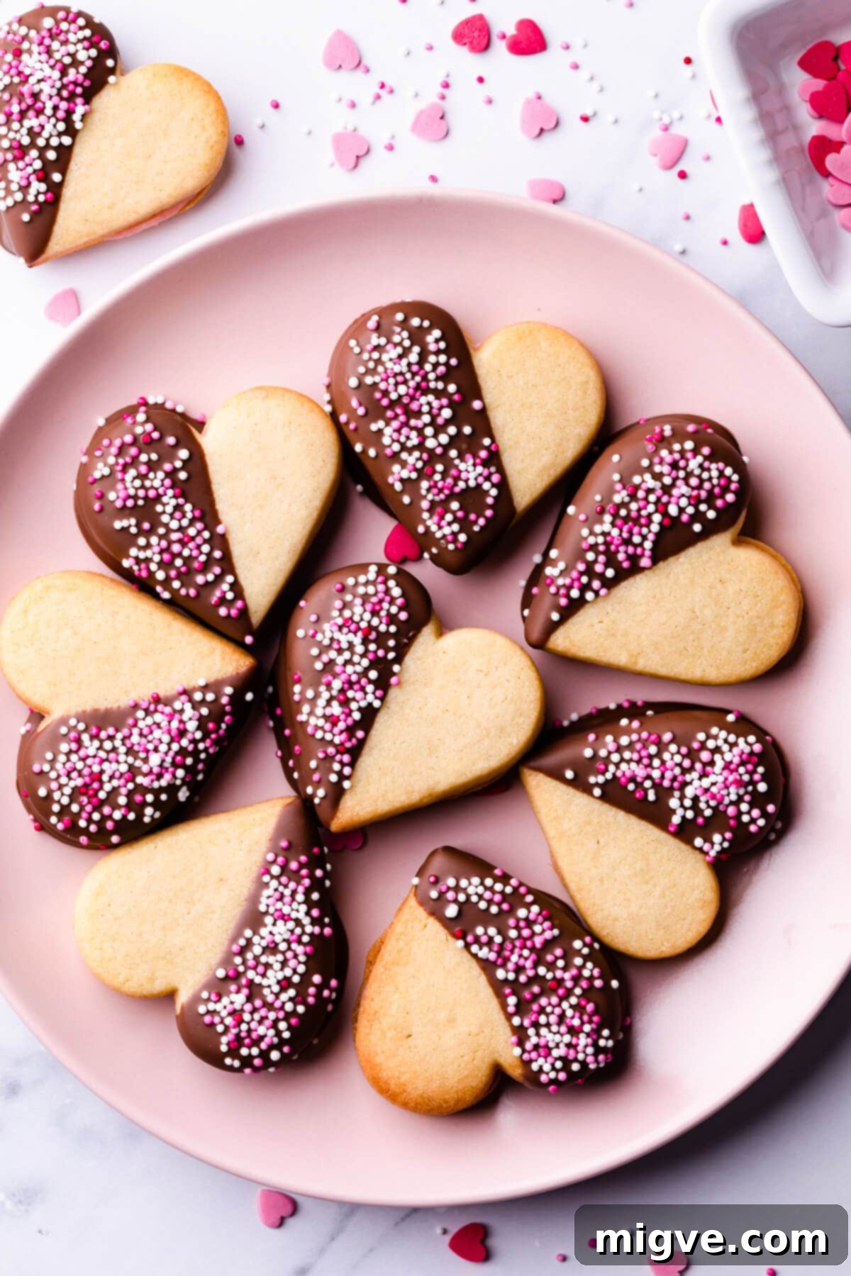 Sweetheart Sugar Cookies 2 Pink plate displaying Valentine sugar cookies, half-dipped in chocolate and topped with vibrant sprinkles.