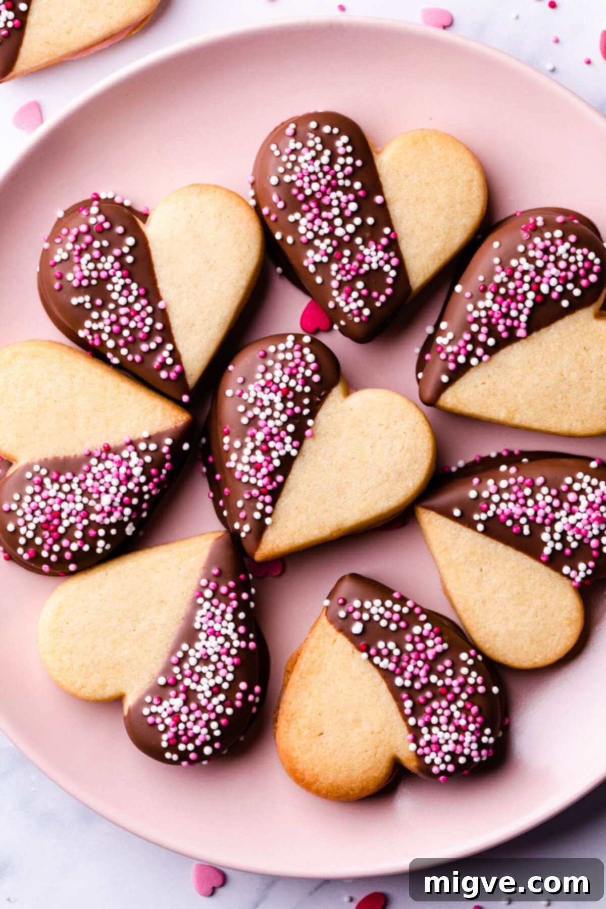 Sweetheart Sugar Cookies 12 Valentine sugar cookies decorated with pink and white sprinkles, arranged on a pink plate.