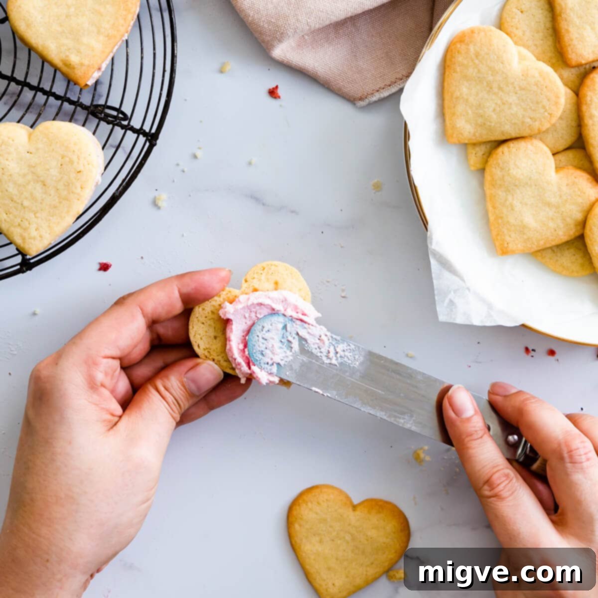Sweetheart Sugar Cookies 6 Raspberry whipped cream filling being carefully spread onto the flat side of a sugar cookie.