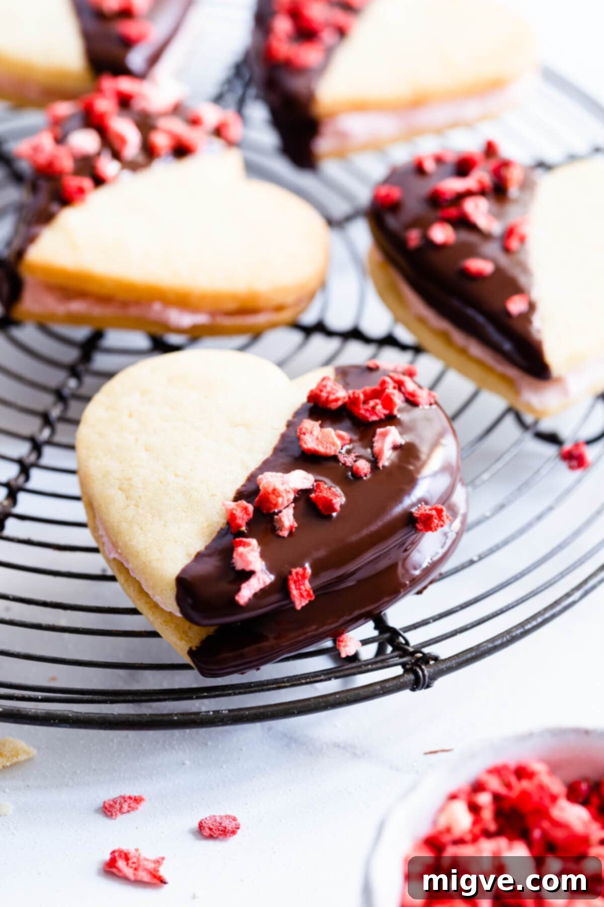 Sweetheart Sugar Cookies 9 A single heart sandwich cookie topped with freeze-dried strawberries, resting on a cooling rack.