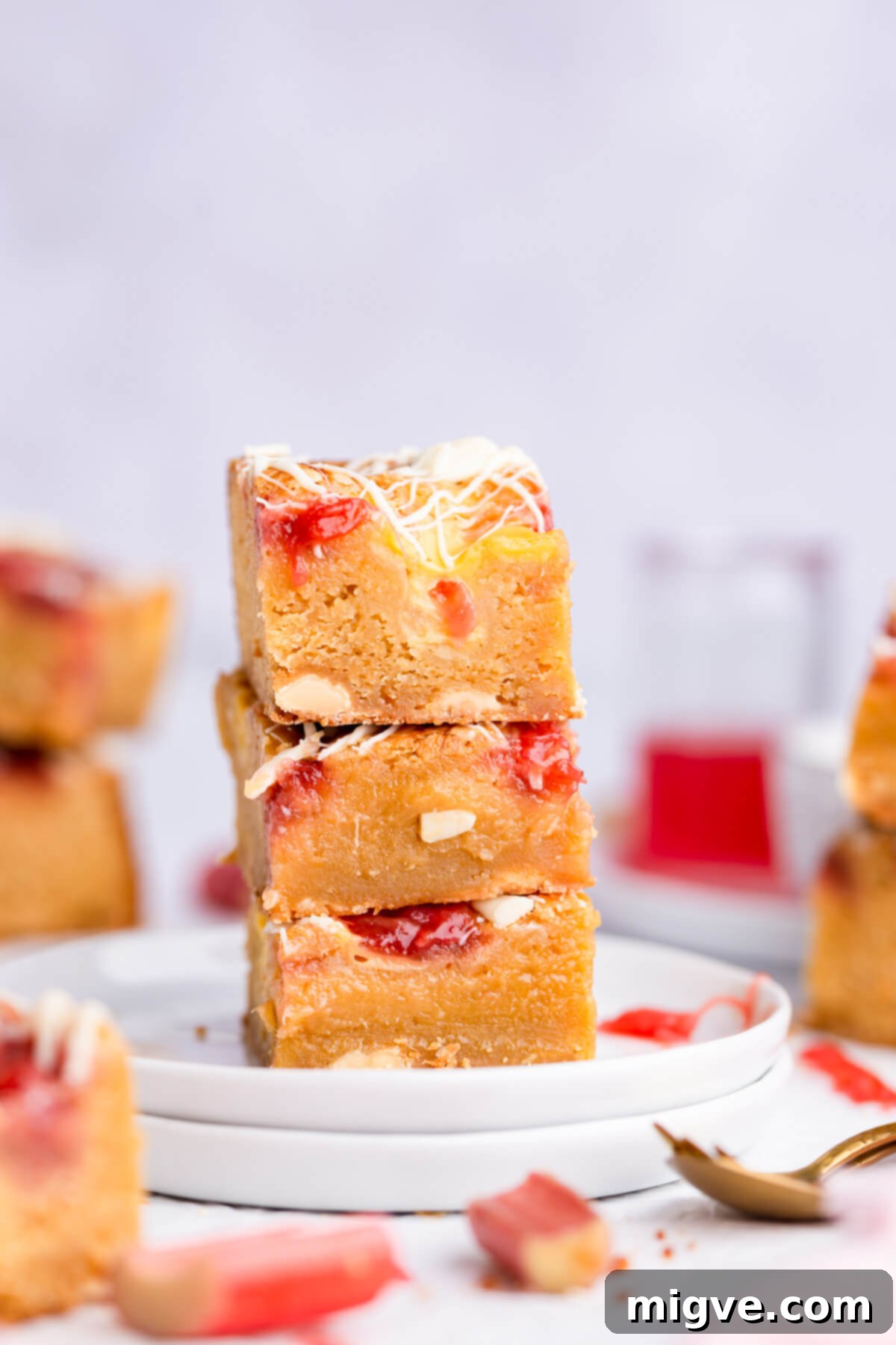 Close-up shot of three delicious rhubarb and custard blondies stacked on top of each other, showcasing their layers and white chocolate drizzle.