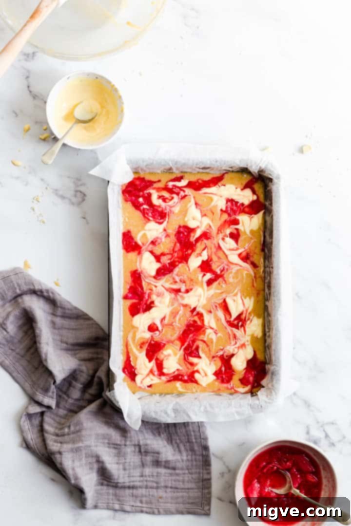Top view of blondie batter beautifully topped with artful swirls of rhubarb compote and creamy custard, creating a stunning marble effect, ready for the oven.