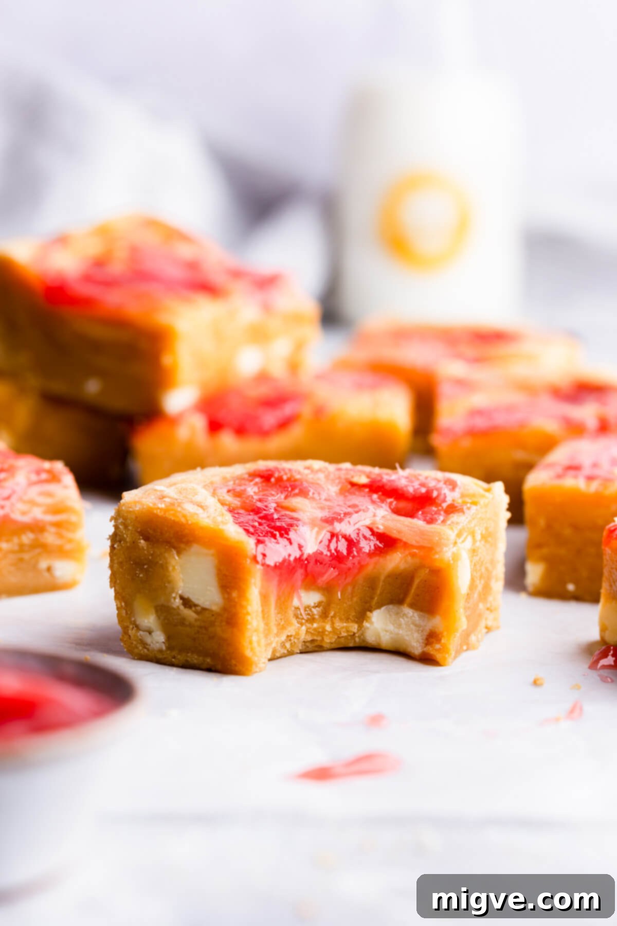 Straight-ahead super close-up of a square slice of rhubarb blondie cake with a bite taken out, showing the gooey interior, white chocolate chunks, and marbled topping.