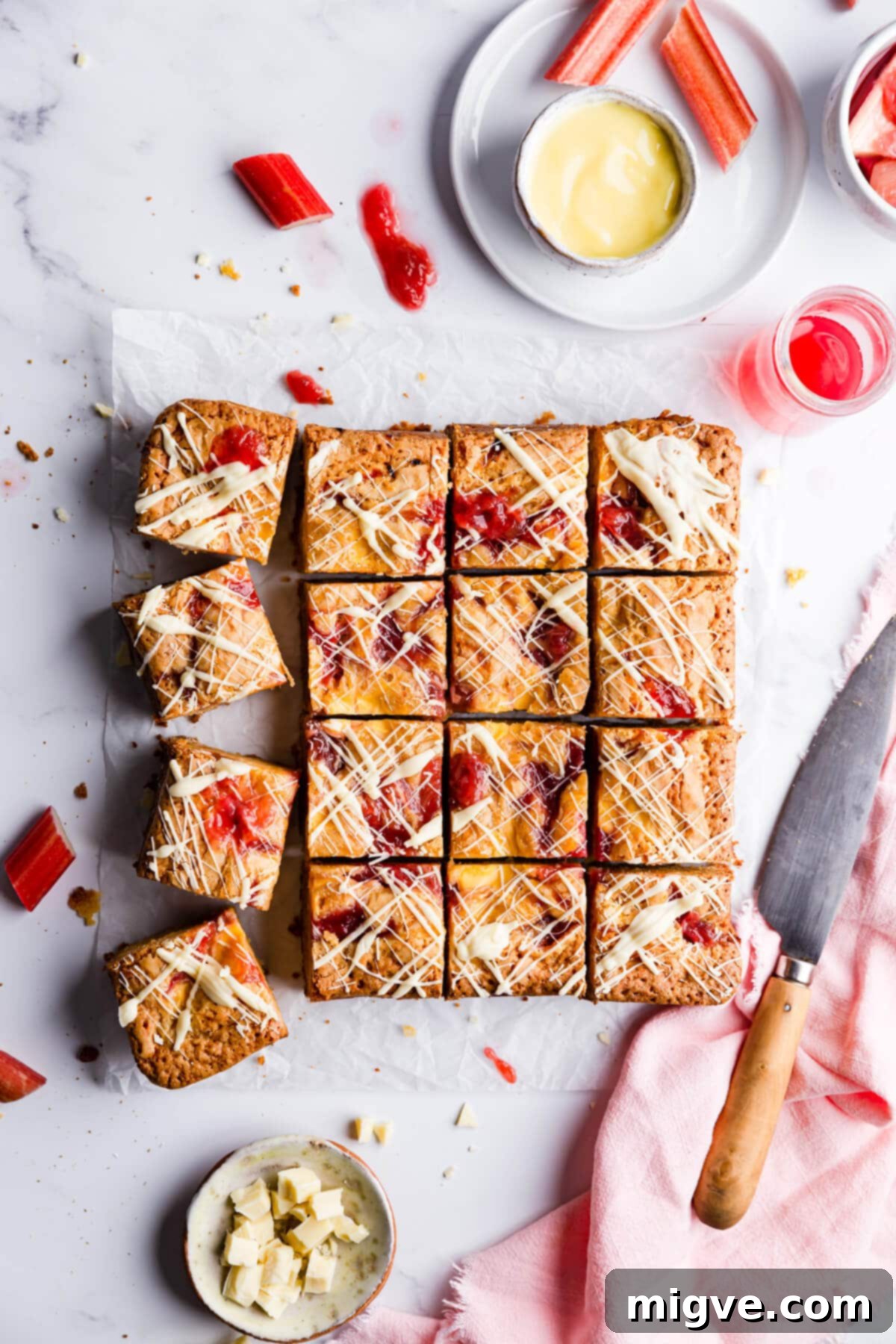 Overhead close-up of rhubarb and custard blondies neatly cut into sixteen perfect squares, ready to be served on a rustic wooden board.