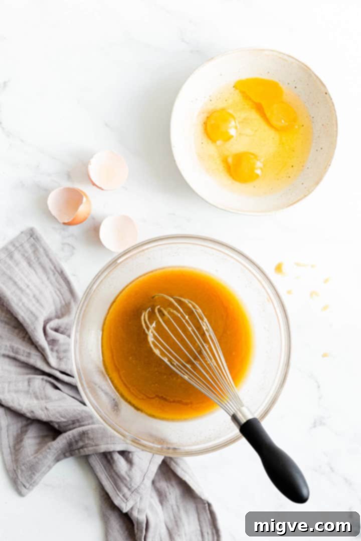 Top view of separate bowls, one containing the golden melted butter and sugar mixture, and another with whisked eggs, at room temperature and ready to be combined.