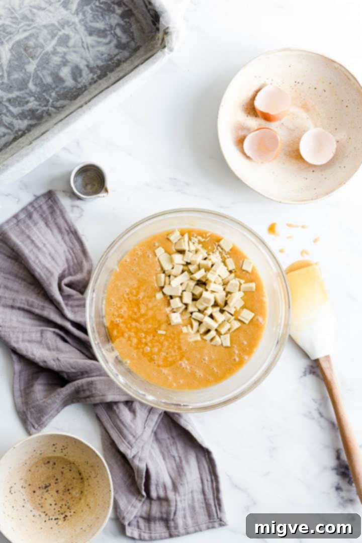 Top view of a bowl containing thick, golden blondie cake batter, with generous white chocolate chunks folded in, ready for assembly.