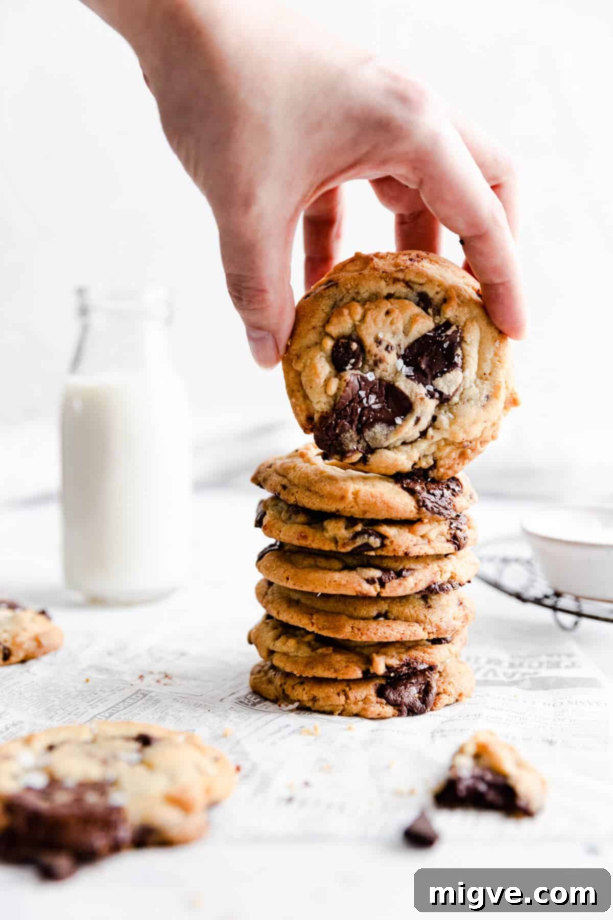 side view of a person lifting a cookie from a stack of freshly baked chocolate chip cookies