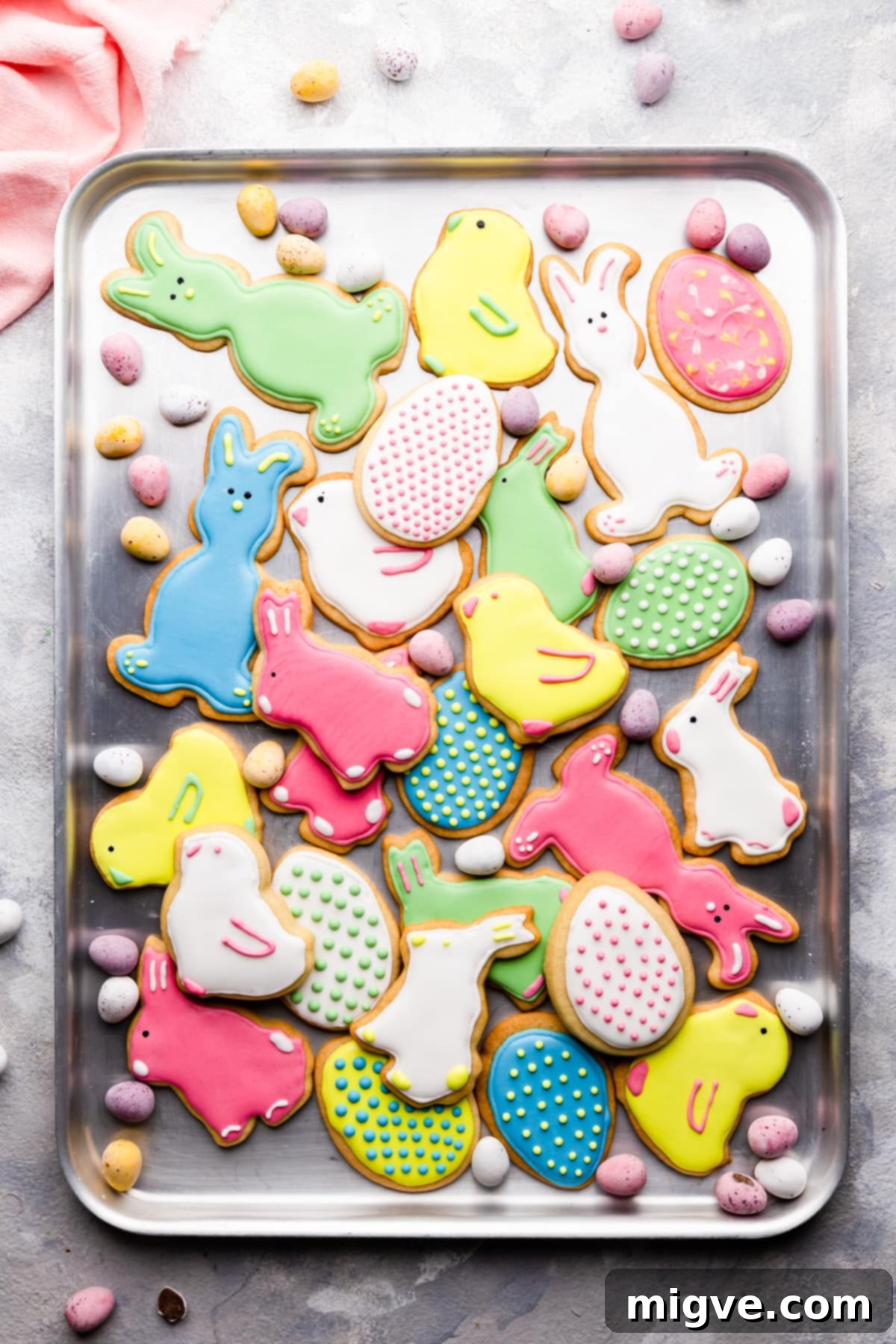 A beautiful top view of freshly baked Easter sugar cookies, some decorated with royal icing, laid out on a baking sheet to cool.