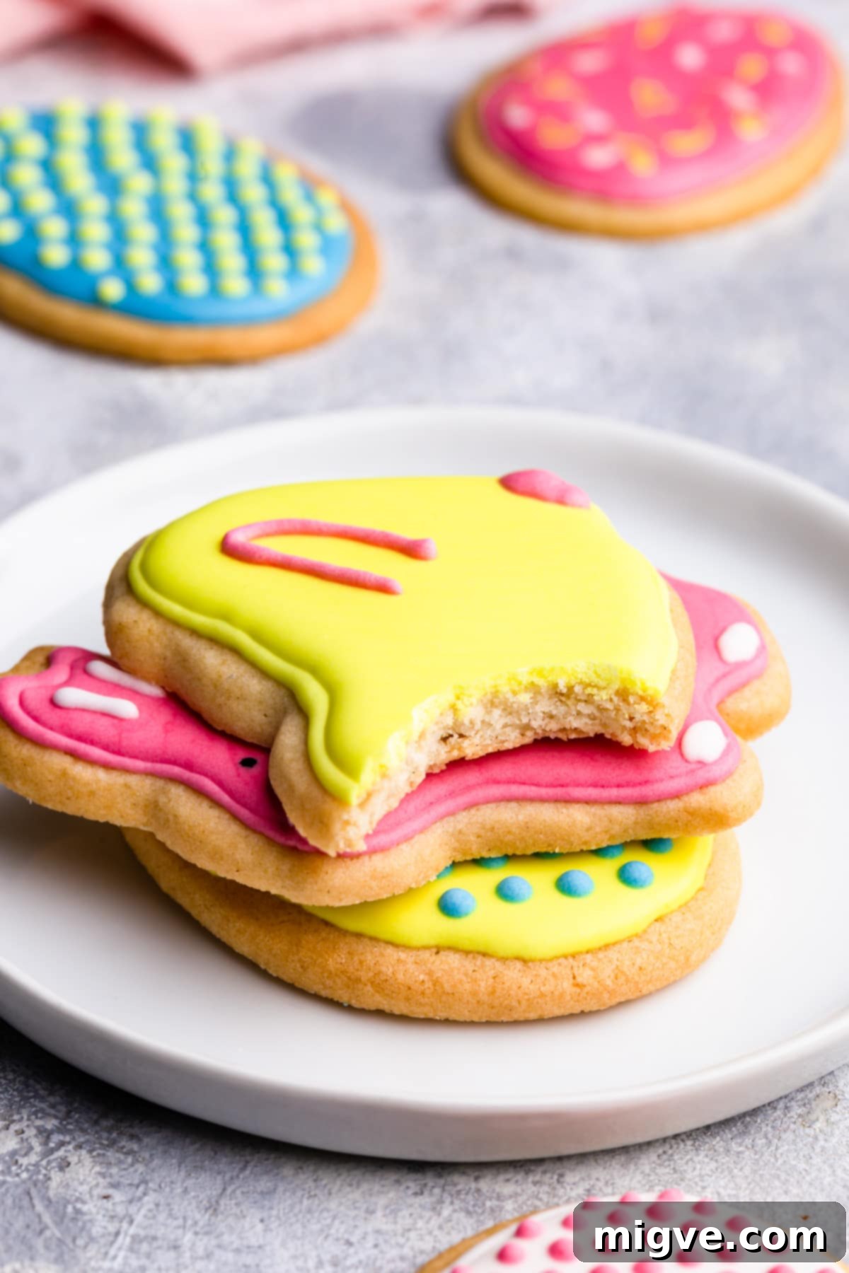 A close-up side view of a stack of golden sugar cookies, one with a bite missing, showcasing their soft interior and lightly browned edges.