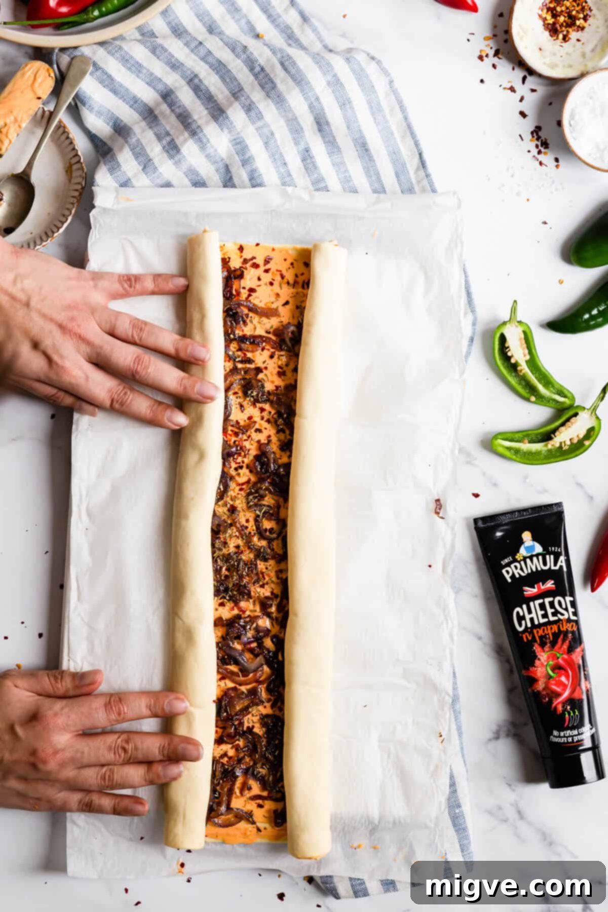 top view of person rolling side of puff pastry sheet towards the middle