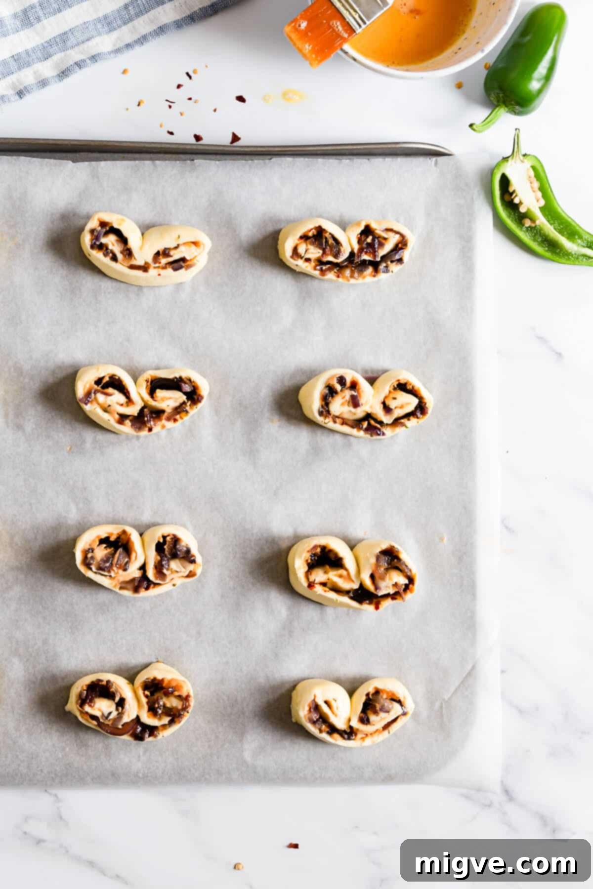 overhead shot of slices of puff pastry with cheese ad onion on a baking tray 
