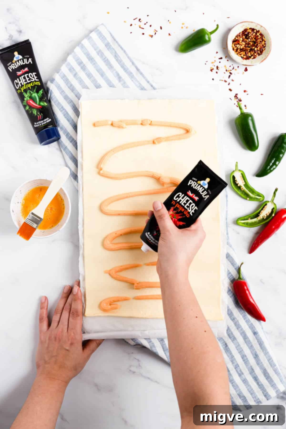 overhead process shot of a person squeezing soft cheese on puff pastry sheet
