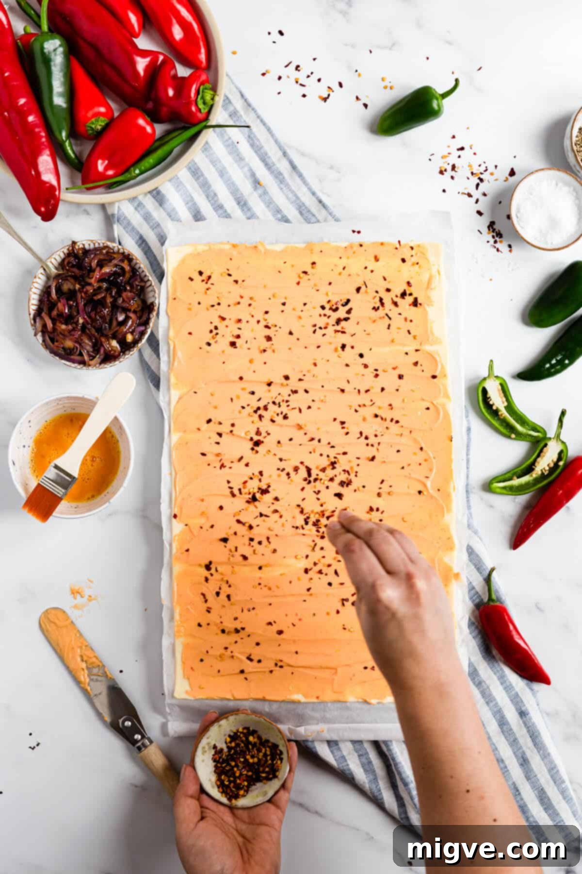 overhead shot of a person sprinkling chilli flakes over puff pastry with cheese