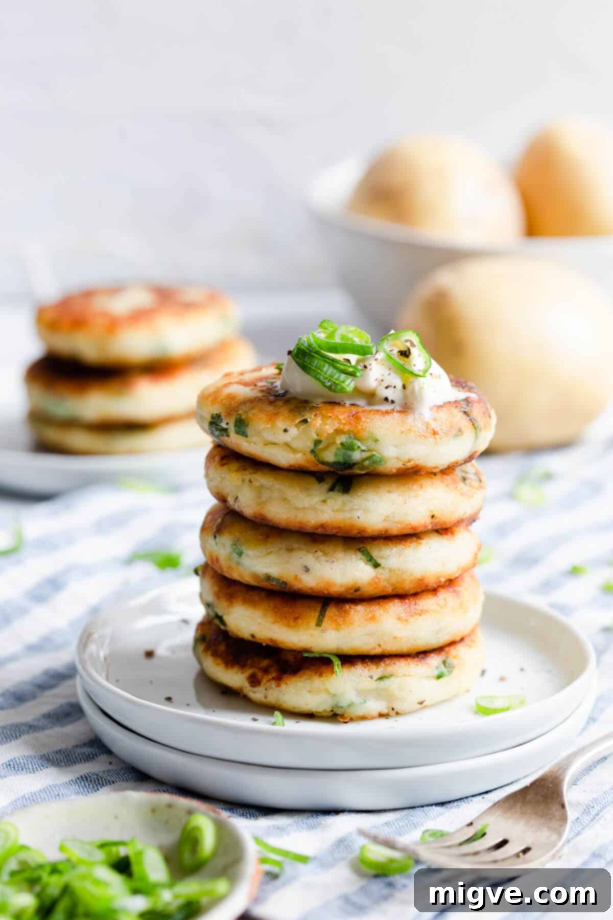 A perfectly stacked pile of golden-brown potato patties with fresh chives on a white plate, ready to be enjoyed.