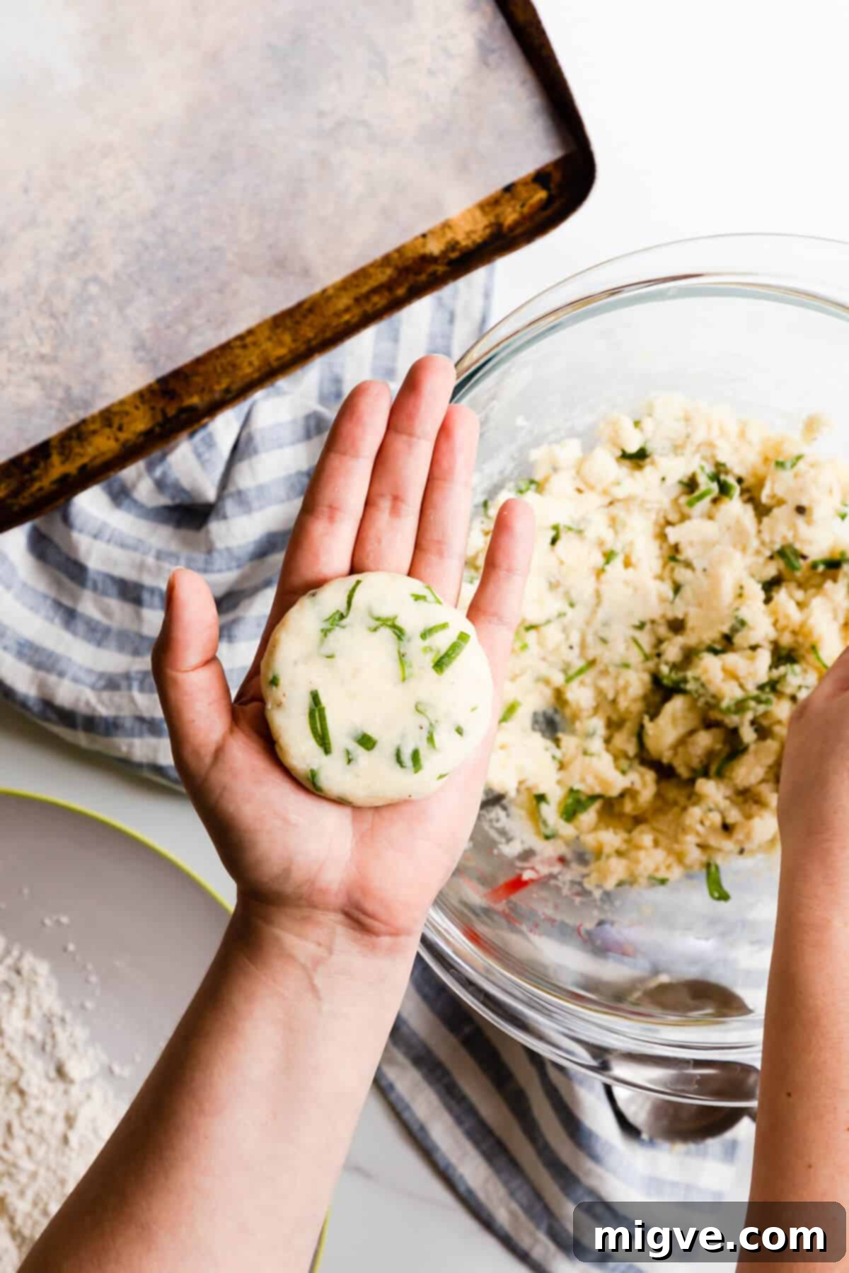 Top view of a hand gently shaping a potato patty, showcasing the ideal size and consistency before flouring.