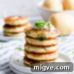A perfectly stacked pile of golden-brown potato patties with fresh chives on a white plate.