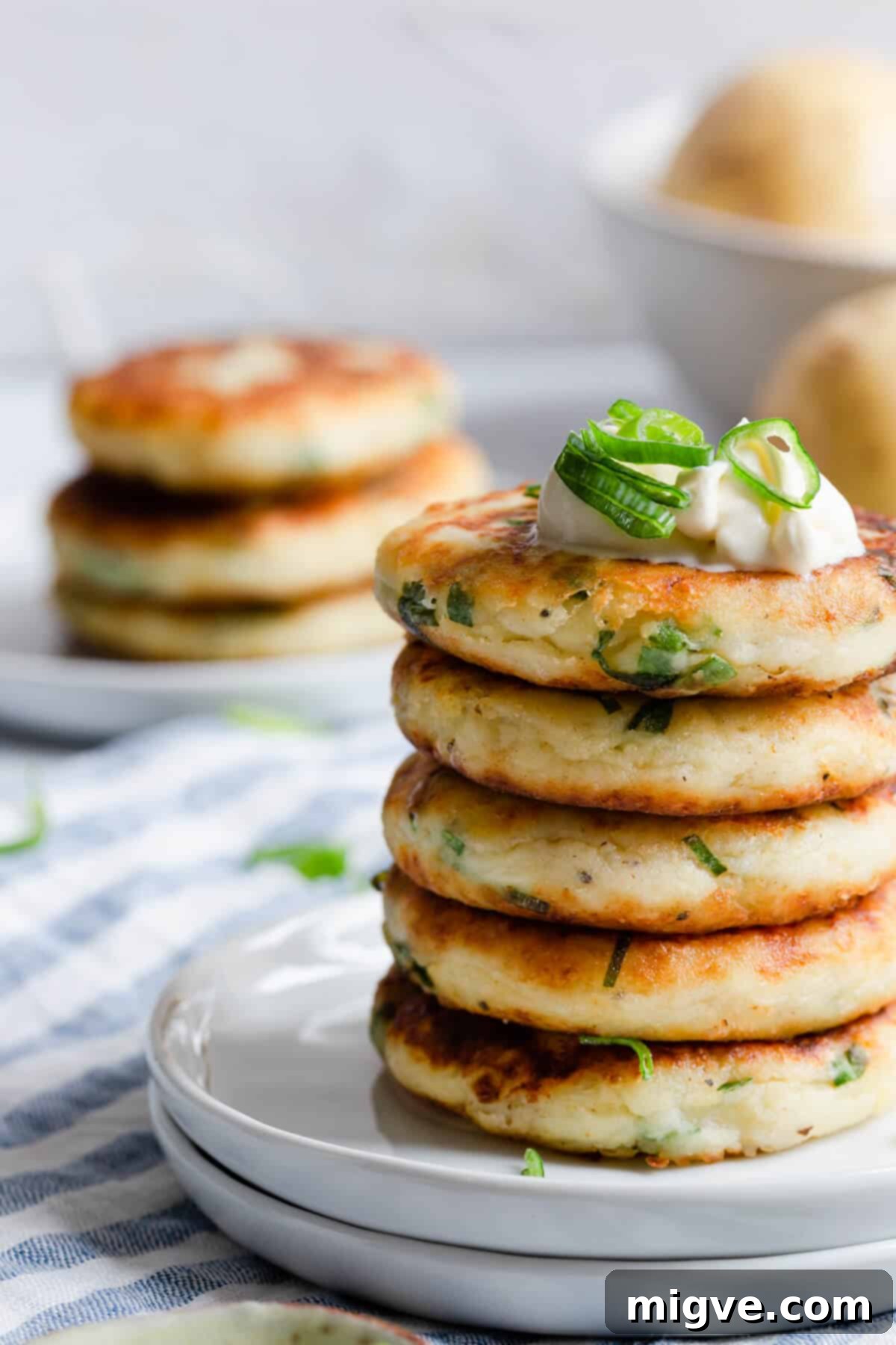 Close-up side view of several crispy potato patties generously garnished with fresh green chives, artfully arranged on a clean white surface.