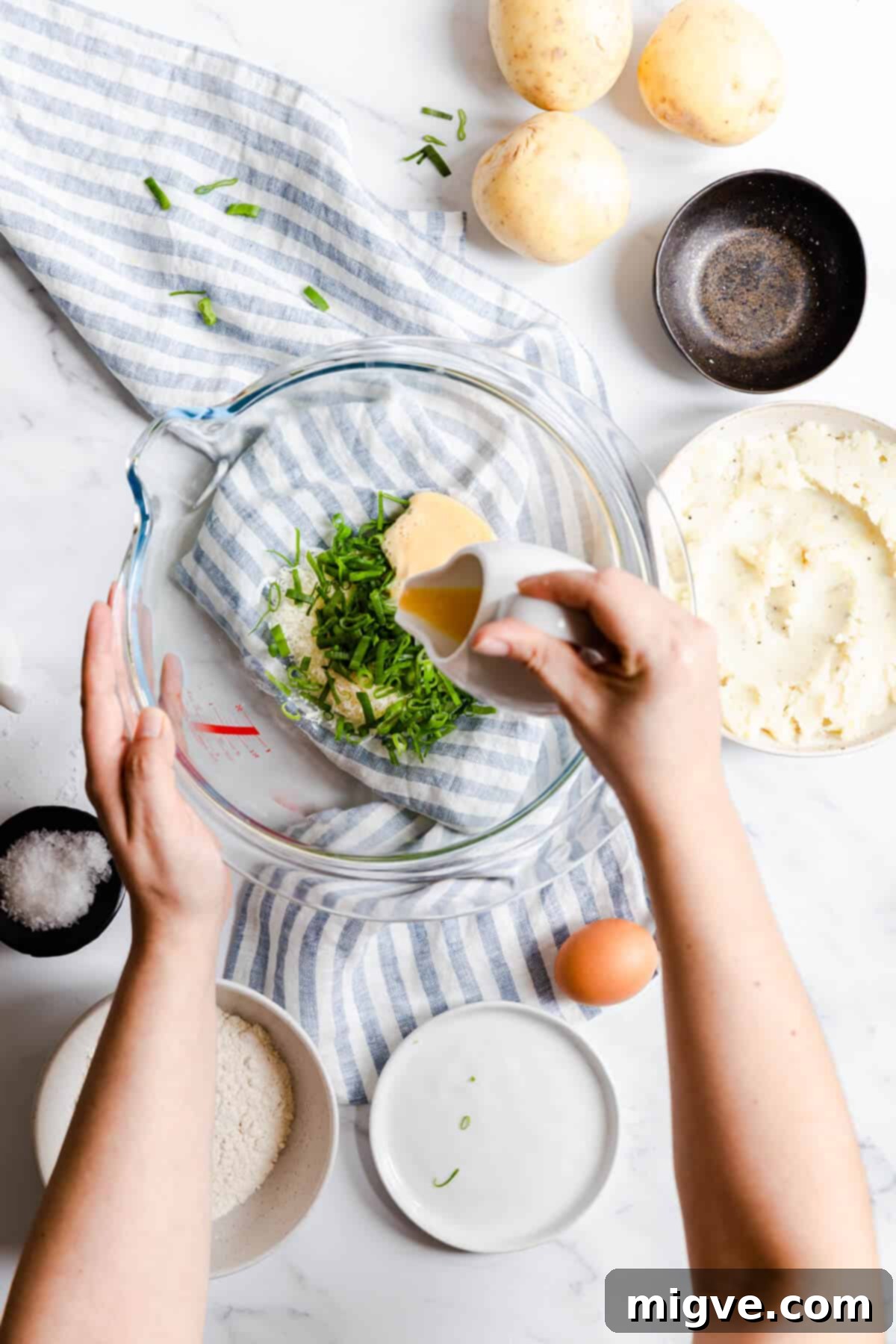 Top view of a hand pouring a beaten egg into a bowl filled with cheese and chives, combining the ingredients for potato patties.