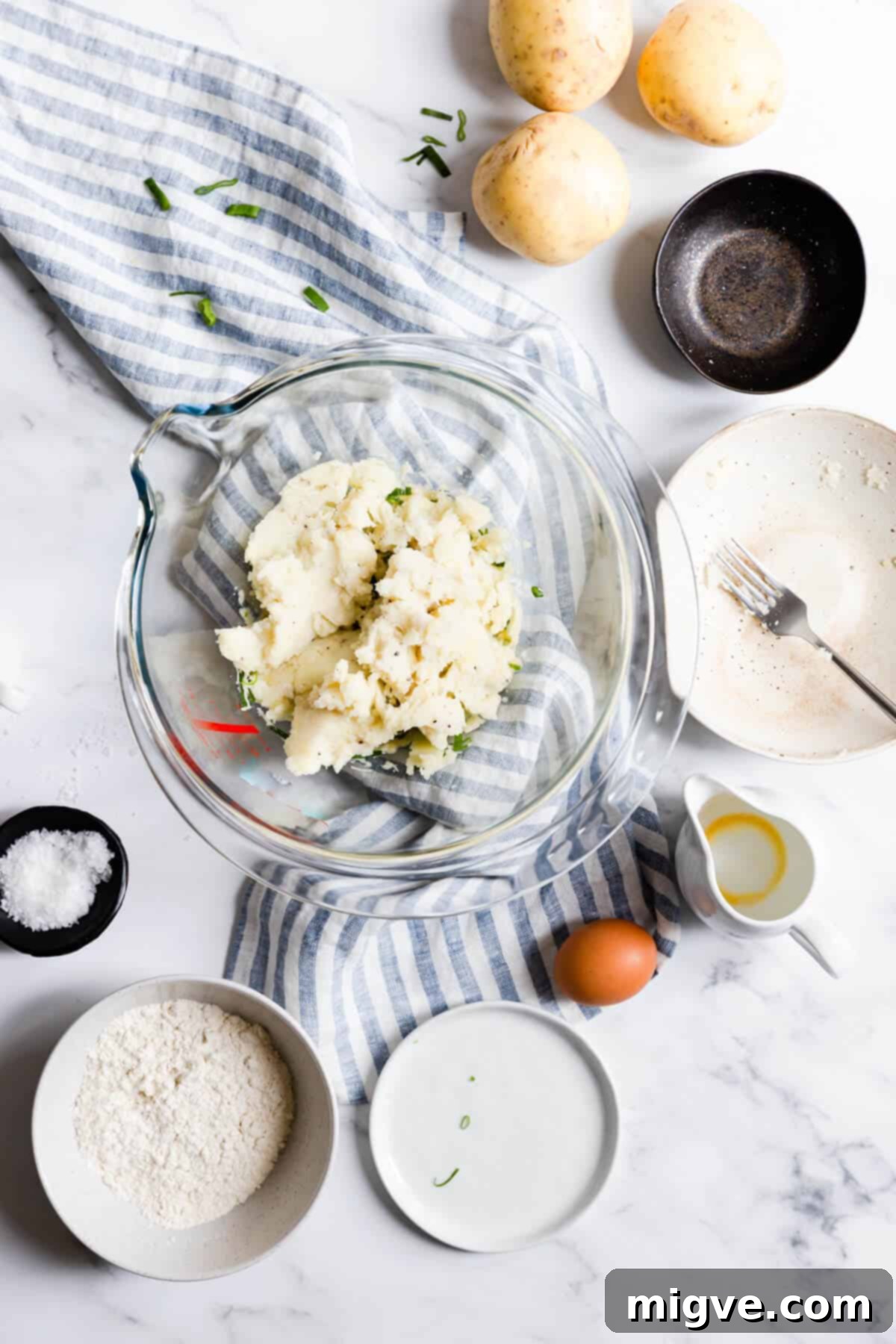 Top view of a bowl showcasing the combined mixture for potato patties, including mashed potatoes, cheese, chives, and egg, before chilling.
