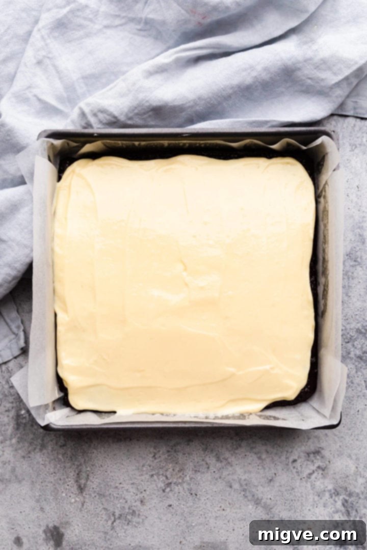 top view of baking tin with cheesecake layer batter on top of the brownie batter